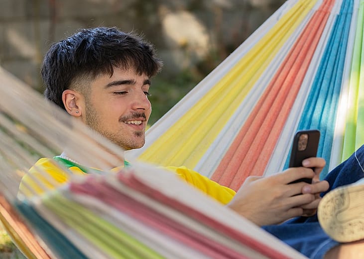 A happy young man in a hammock using his smartphone.