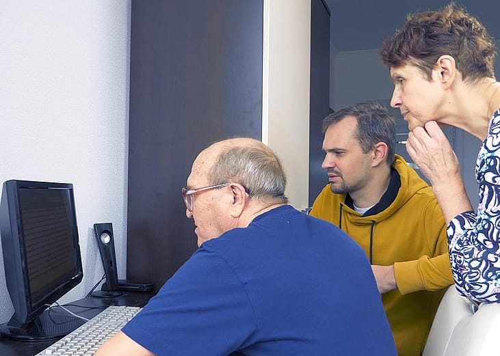 Senior parents using a computer at home guided by their adult son.