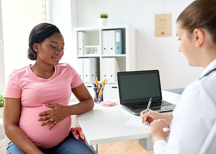 A pregnant black woman consulting with her doctor in a clinic.