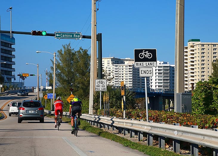 Two cyclists travel north in a bike lane toward the Real Intracoastal Waterway Bridge in Florida, USA.