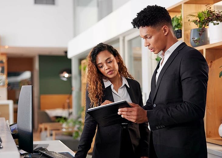A pair of hotel receptionists checking their guest schedule on a digital tablet.