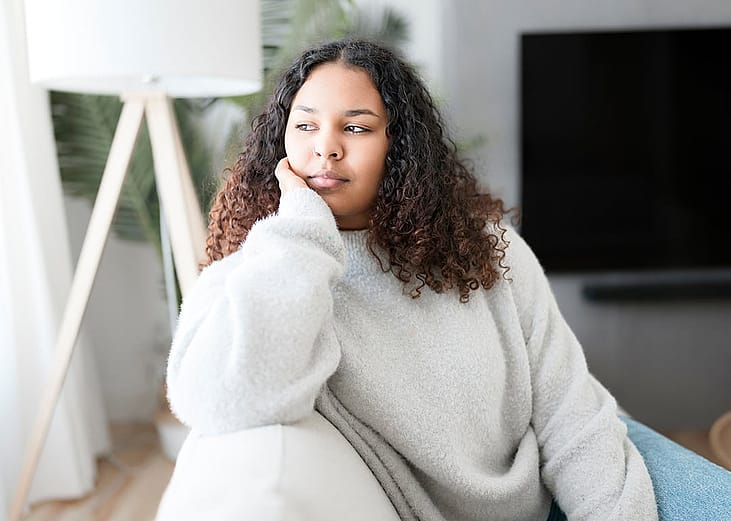 A pensive young woman sitting on the couch at home.