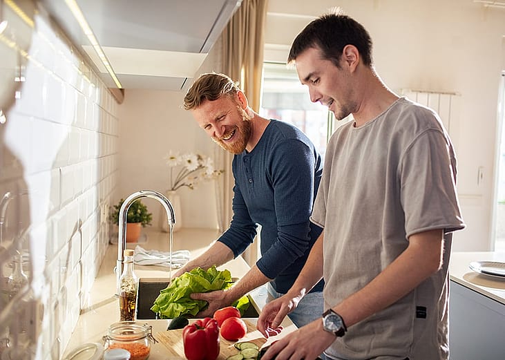 A young gay male couple preparing vegetables in their home's kitchen.