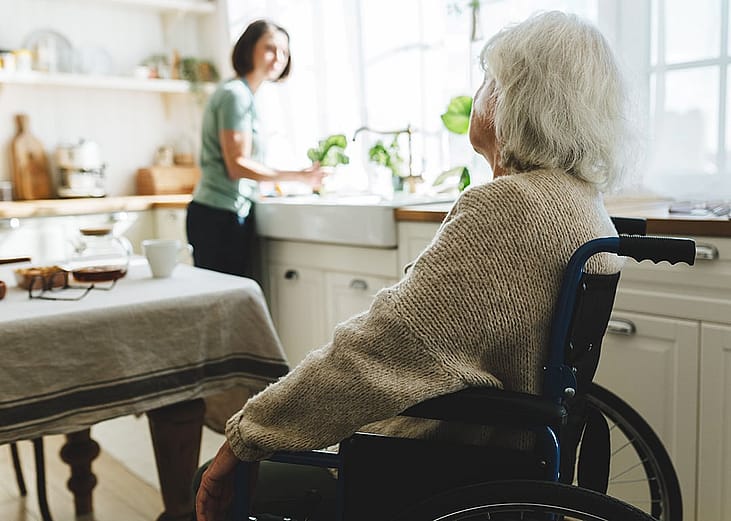 A selective focus shot of an elderly woman in a wheelchair looking at her caregiver at home.