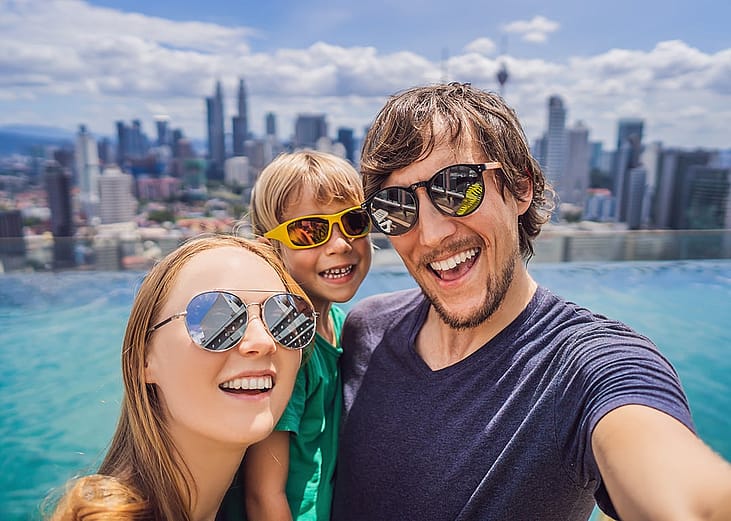A family taking a selfie together with a view of a pool and city sky line.