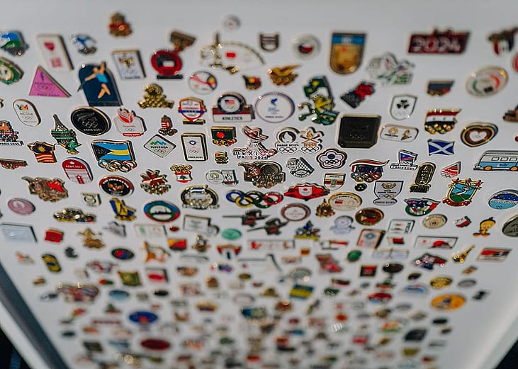 Olympic enamel pins from different countries arranged on a white board showcasing.