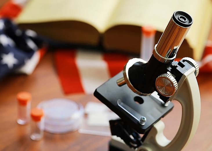 A microscope with an open book and the US flag in the backdrop as a concept of scientific research.