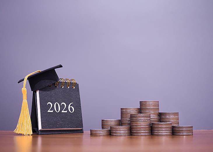 A 2026 calendar with a graduation hat and stacks of coins in a desk.