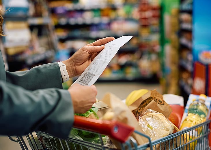 Person looking at a long grocery shopping bill while still at a supermarket.
