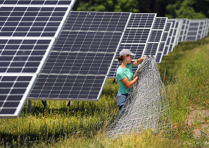 A worker organize fencing materials along solar panels at the Fitchburg Renewables solar farm in Massachusetts.