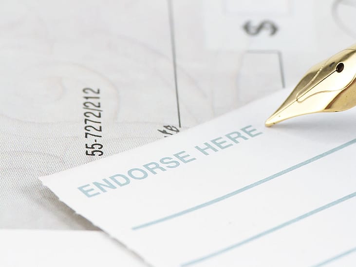 A pen signing an endorsement note to a check.