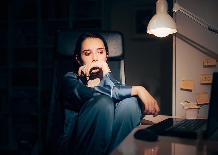 A young woman working at night looking worried staring at her laptop.