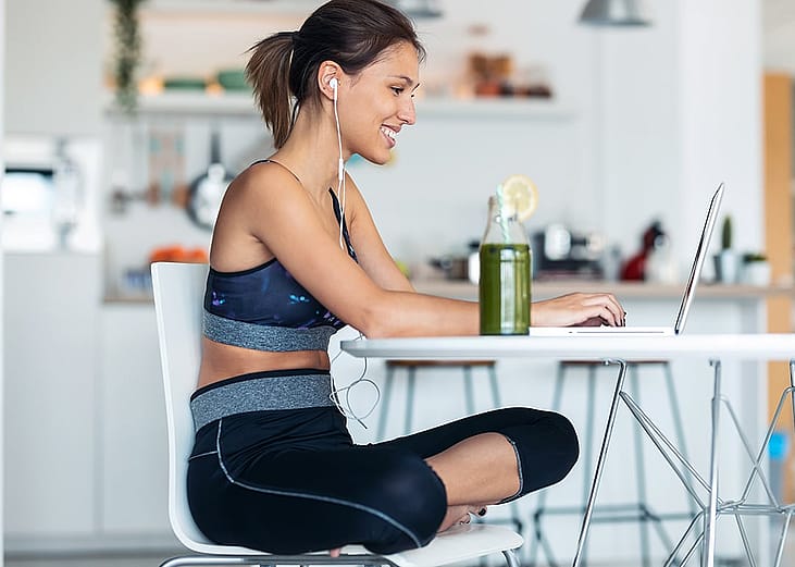 A young woman in athleisure wear working from her home's kitchen.