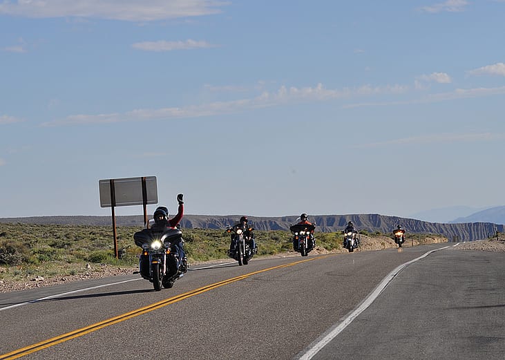Motorbike riders raising hands for a photo opportunity while passing a road in California, USA.
