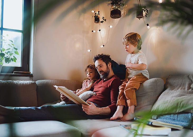 A father with his two children looking at a photo album at home together.