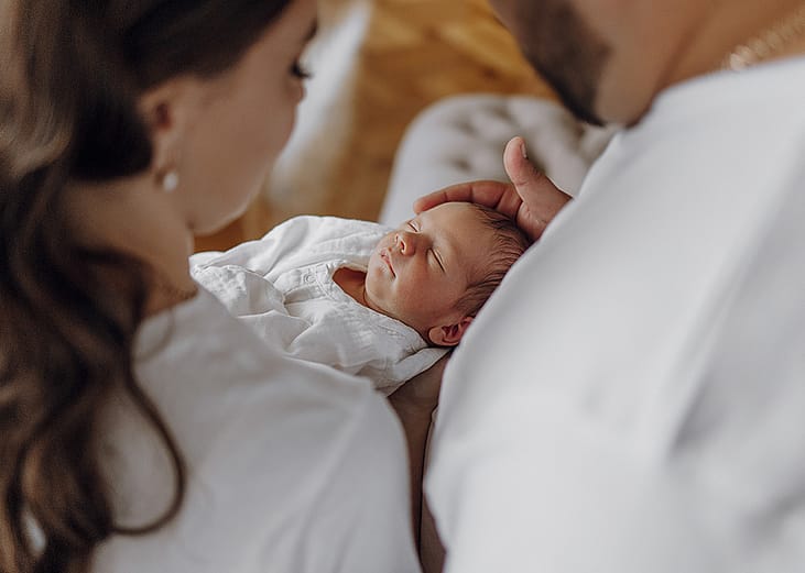 A couple staring at their newborn baby who is sleeping.
