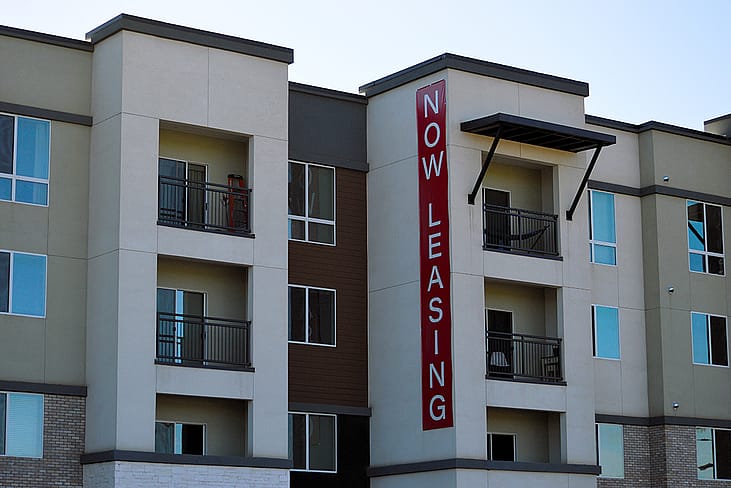 A modern apartment building with a huge 'now leasing' signage.