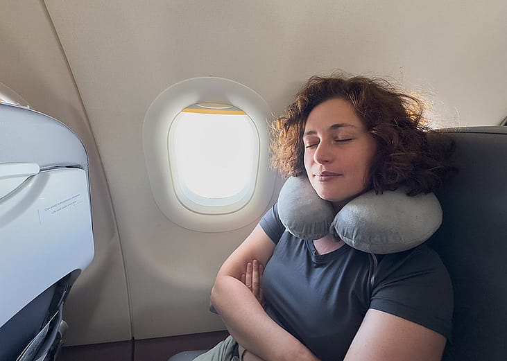 A person sleeping with a neck pillow from her seat in a plane.