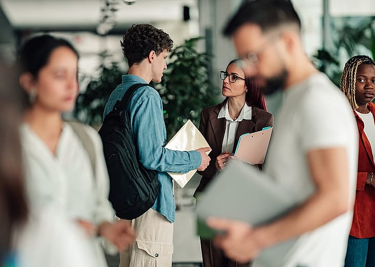 A college student talks to a professor in a campus hallway.