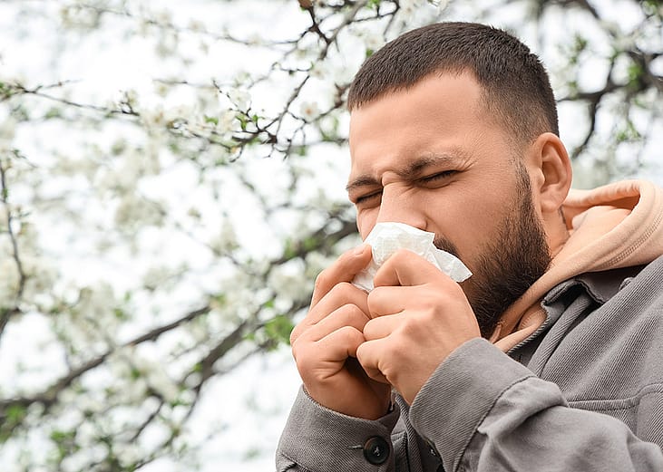 A person sneezing from an allergy outdoors. 