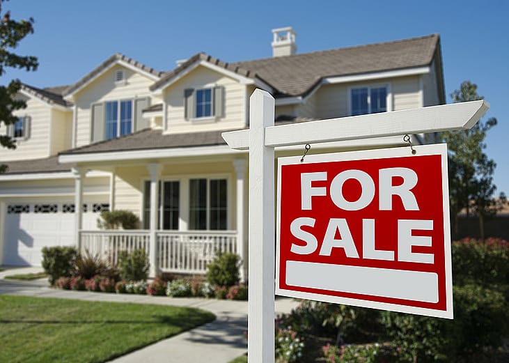 A For Sale sign in front of a residential house.