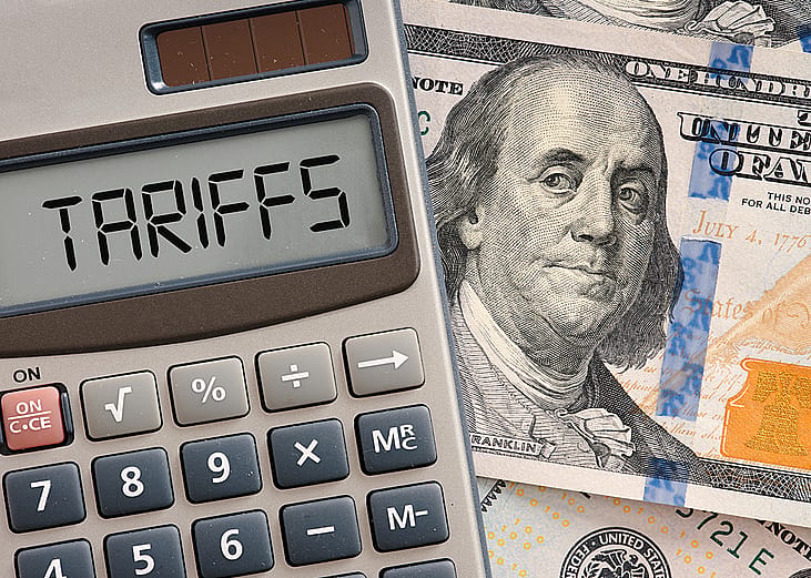 A calculator displaying the word 'tariffs' on top of a US dollar banknote.