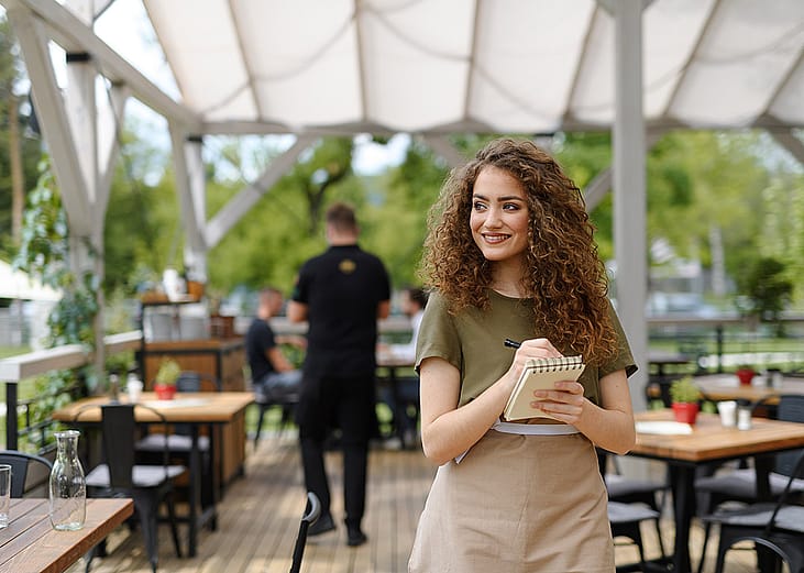 A waitress standing in a restaurant terrace after writing down an order.
