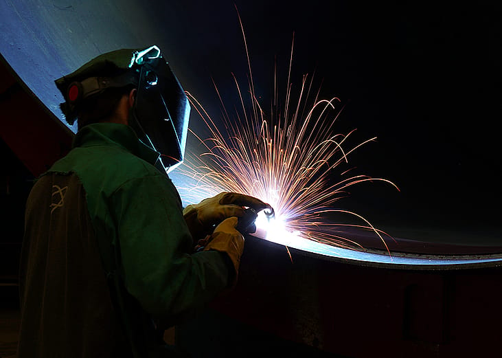 A worker welding a very large steel pipe.