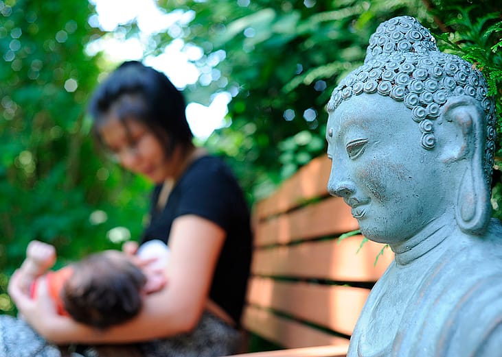 A Buddhist mother carrying and feeding her child outside in a park.