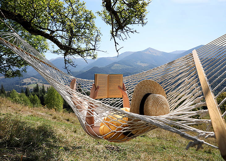 A person reading a book while relaxing in a hammock outdoors.