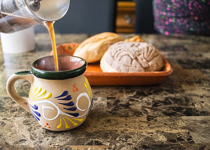 Coffee being poured in a traditional Mexican cup with bread on the side.