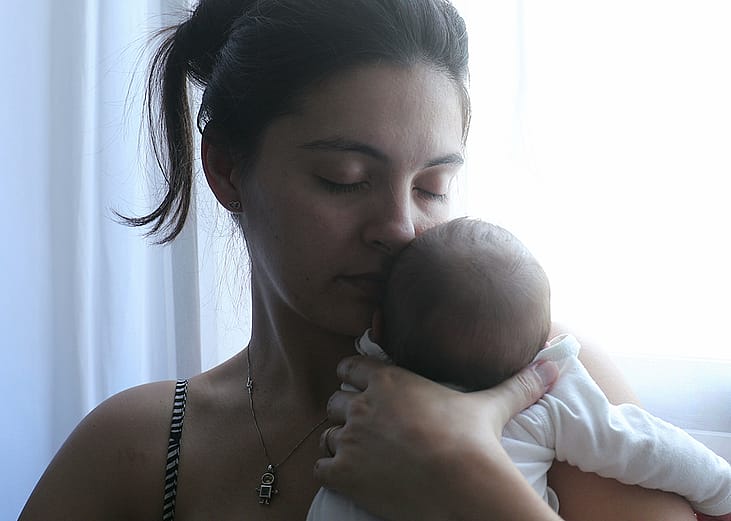 A mother holding her newborn baby by the window.