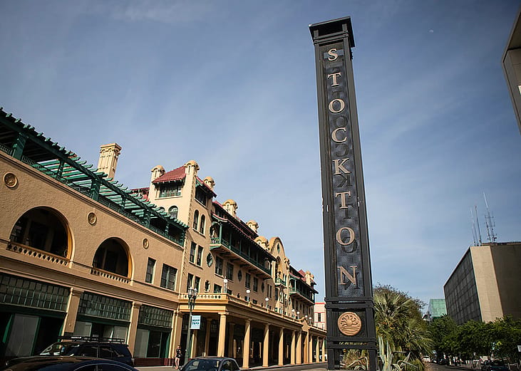 View of a street in downtown Stockton with a tall metallic sign with the city name vertically displayed in 2026.