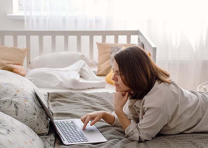 A parent working remotely from a bedroom while her baby toddler is sleeping in a crib.