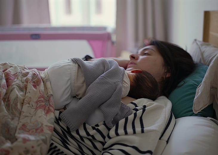 A young mother and her newborn baby napping together at home.