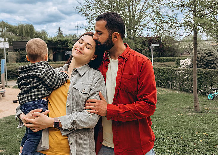 A young family of 3 spending time together outdoors in a park.