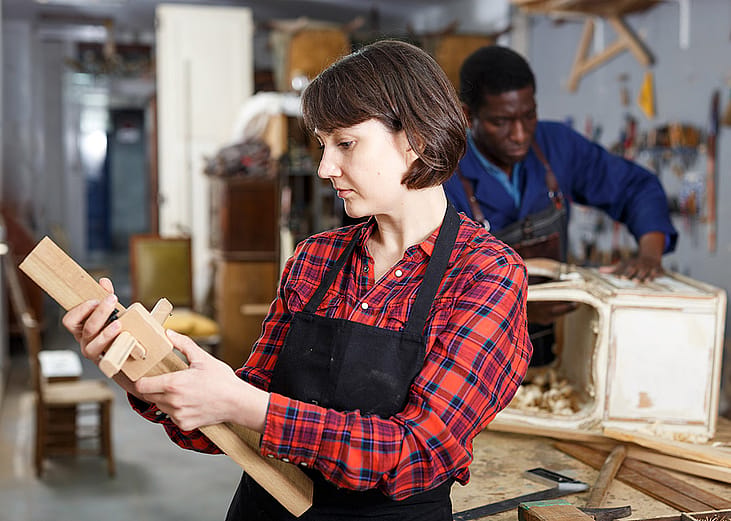 An artisan checking a wood component during a creation process of its furniture in a workshop.