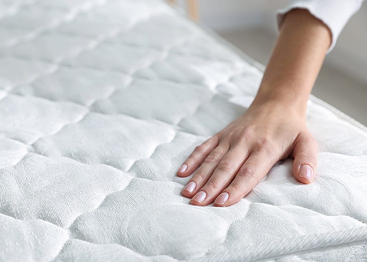 A person touching a bed's soft mattress. 