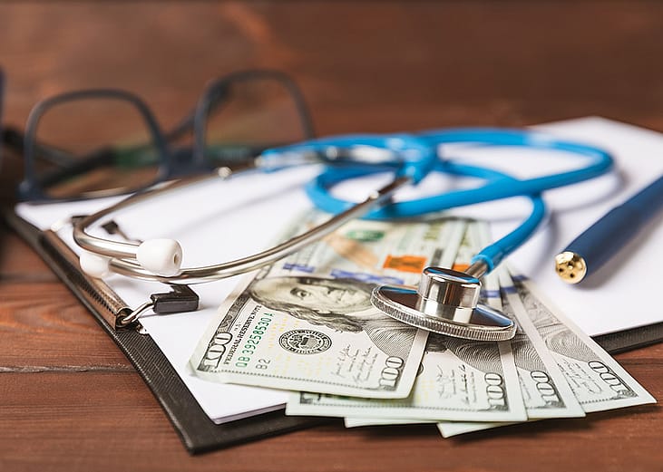 U.S. dollar bills, medical records, and a stethoscope placed in a desk.
