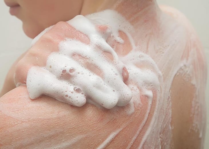 Person exfoliating shoulders with body wash during a shower.