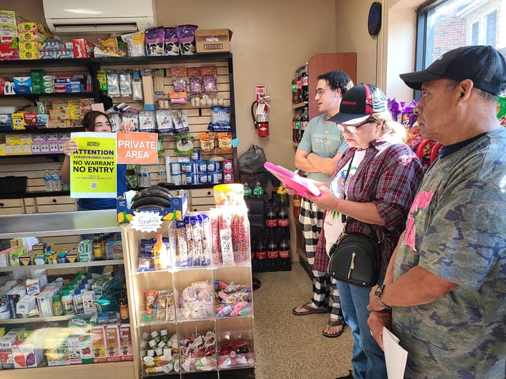 A store worker showing a "No warrant, No entry" / "Private area" signs behind the counter.
