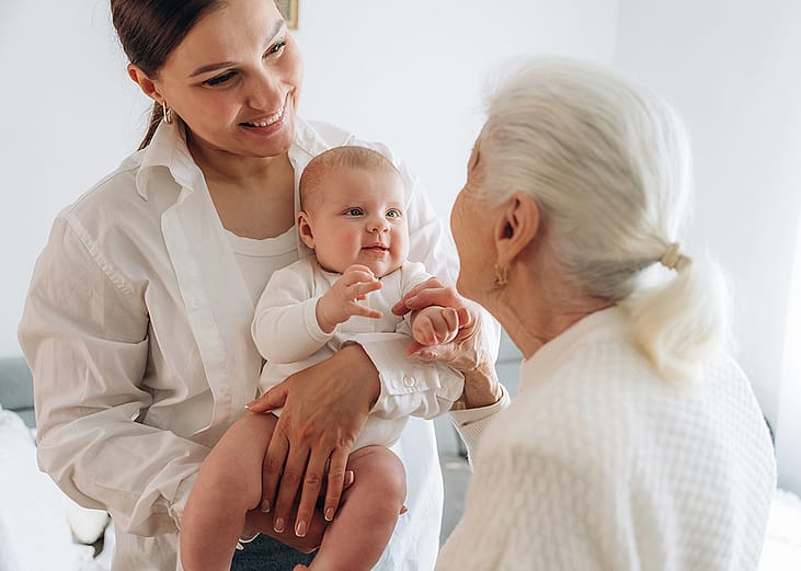 A grandmother looking at her adult daughter and newborn granddaughter.