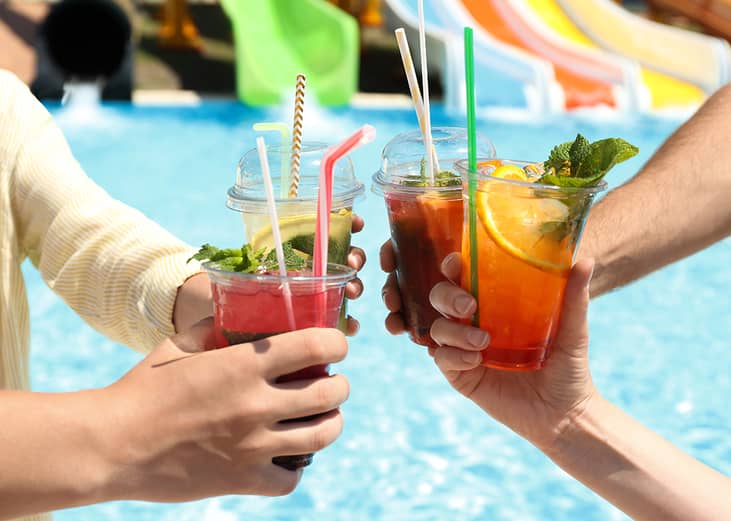 A group of friends putting up their drinks together beside a pool.