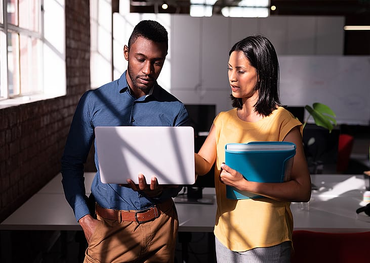 Two colleagues standing in an office discussing a task together.