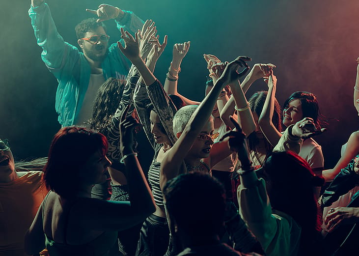 A crowd raising their hands as they dance under the lights in a club.