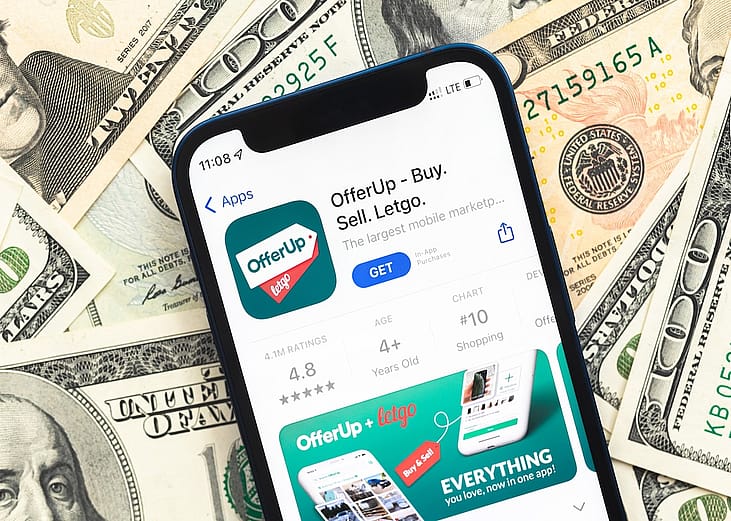 An OfferUP shopping app logo displayed from a mobile phone screen with U.S. dollar bills in the background.