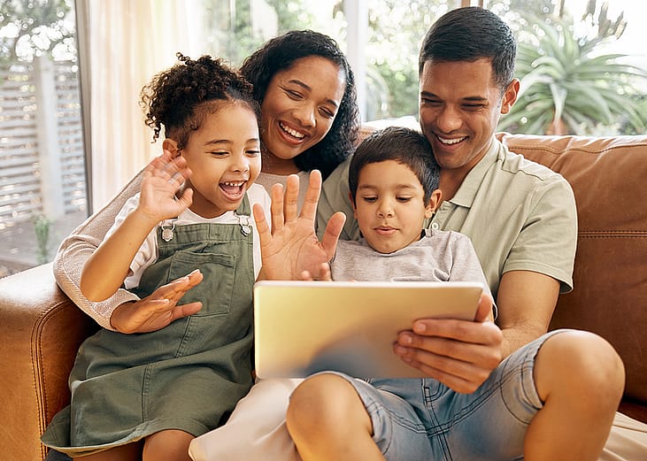 A family greeting and smiling to their relatives through a video call from a tablet at their home.