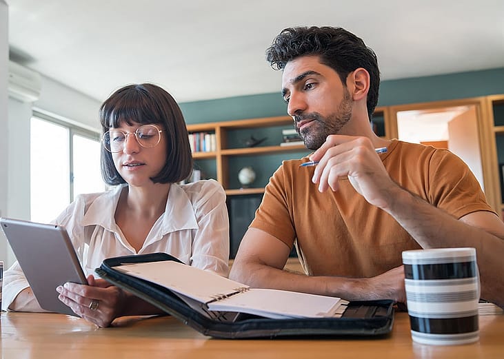 A young couple reviews and pays bills online using a digital tablet.