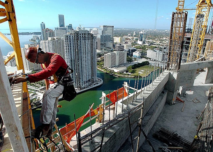 A construction worker makes his way up the side of a condominium highrise construction site in downtown Miami, Florida.