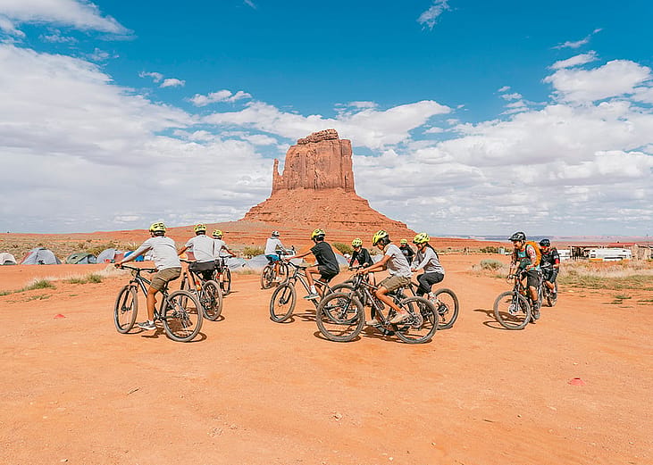 A cycling group in the Arizona desert, specifically within Monument Valley.